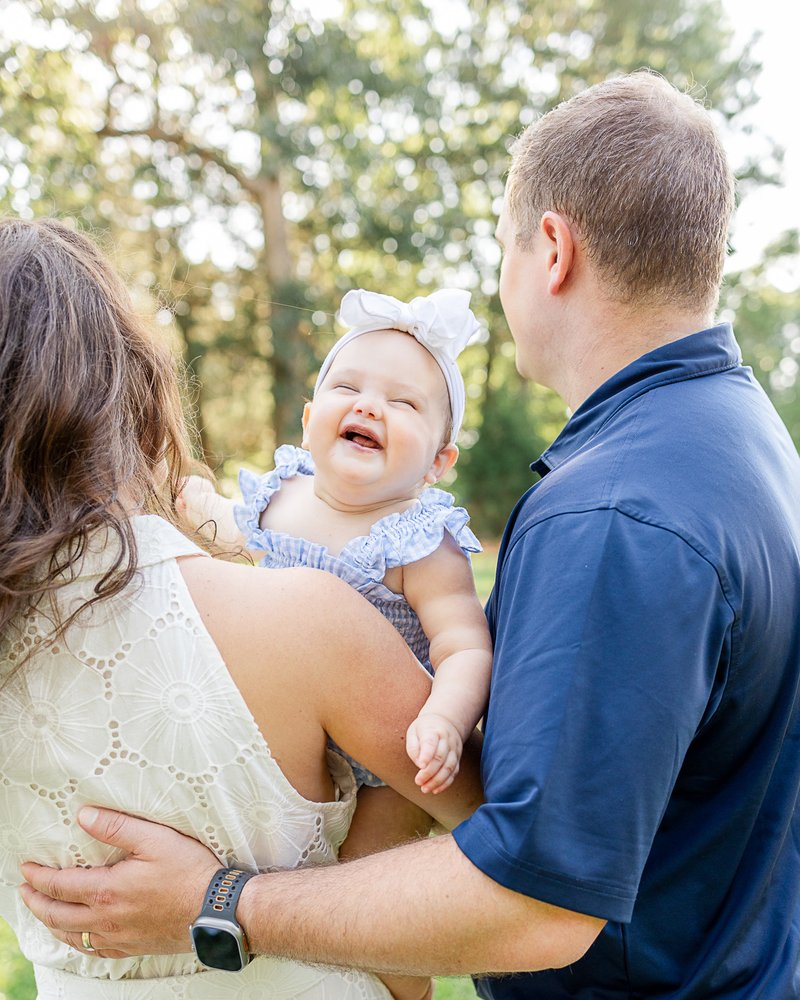 Parents laughing with their smiling baby girl outdoors