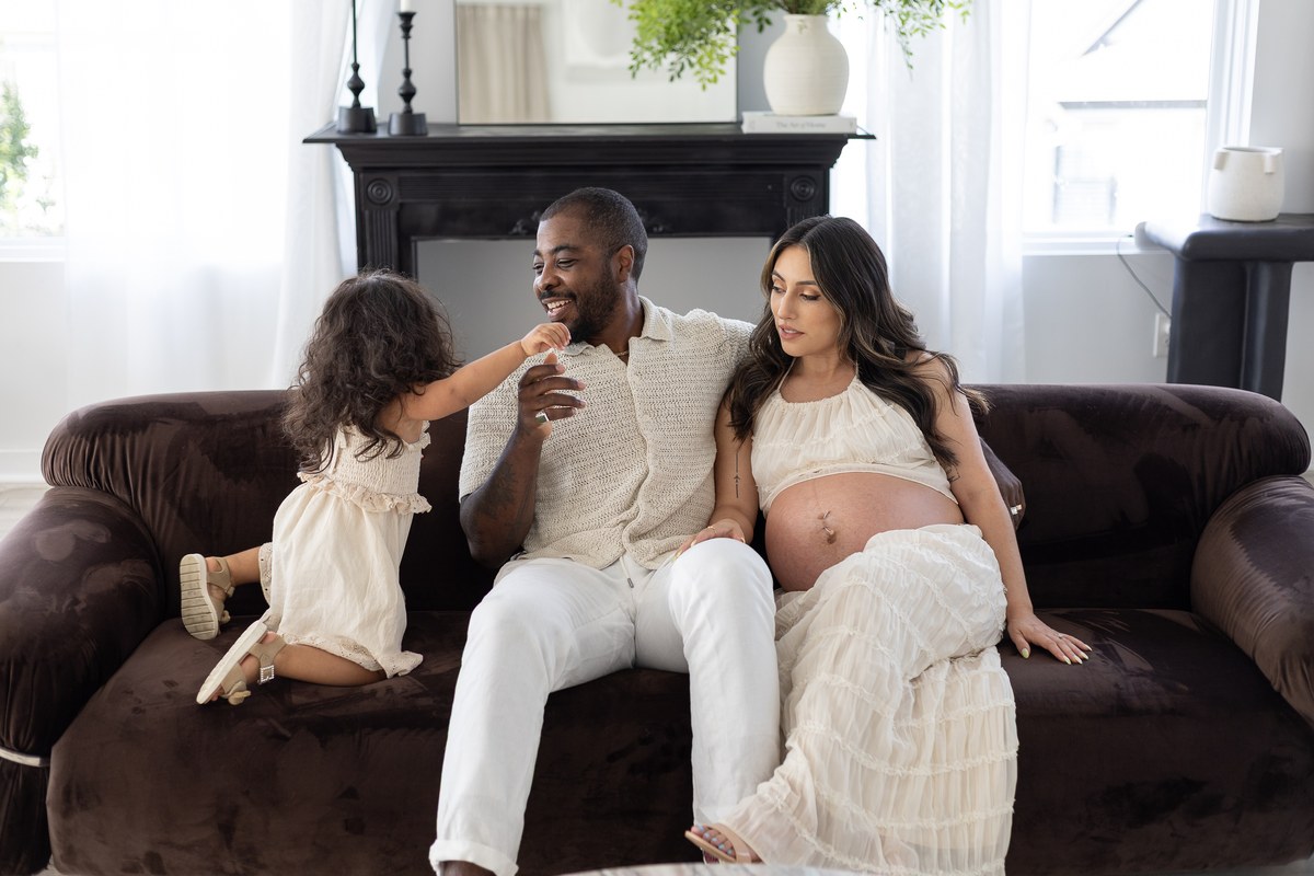 Expectant parents and their daughter relaxing together on a velvet sofa