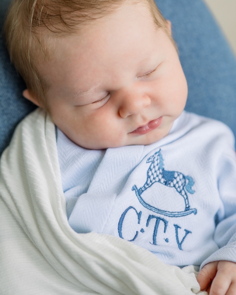 Newborn sleeping with a soft smile in a pale blue shirt