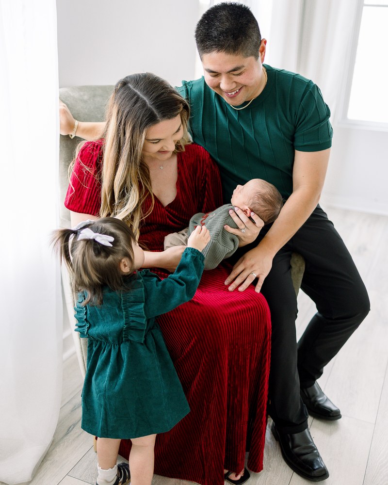 Parents and older sister gathered around their newborn in a bright holiday studio