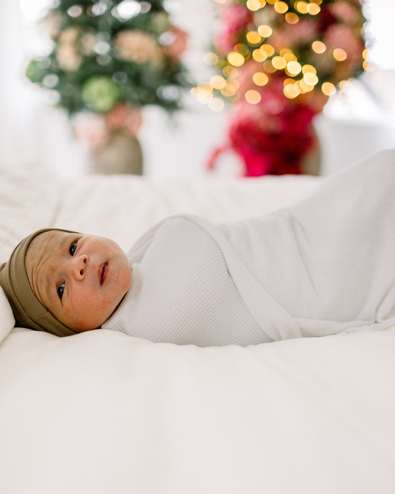 Swaddled newborn lying awake beneath soft holiday lights