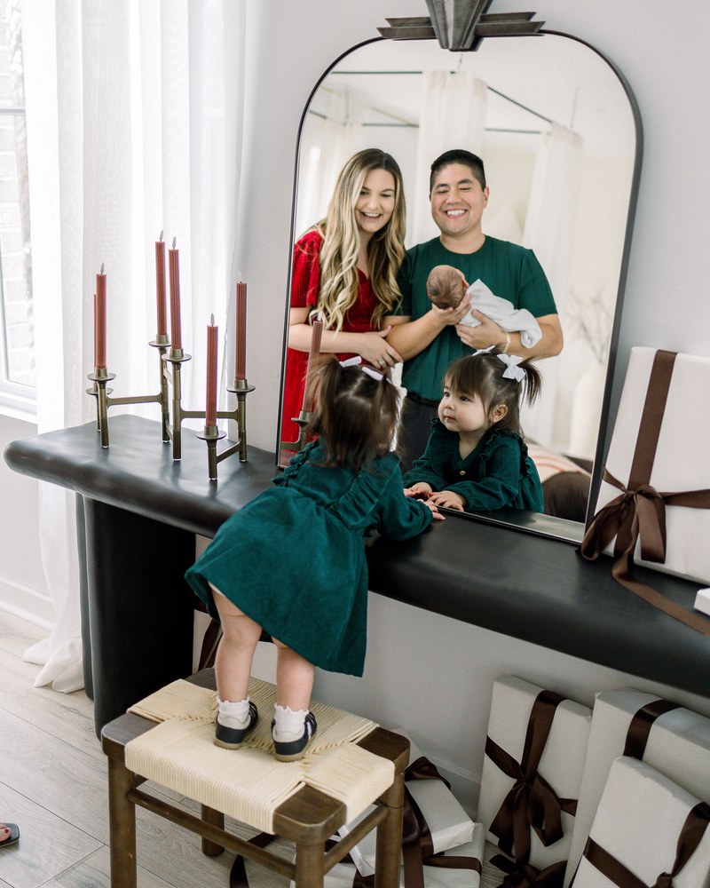 Older sister looking in the mirror while her parents hold their newborn behind her