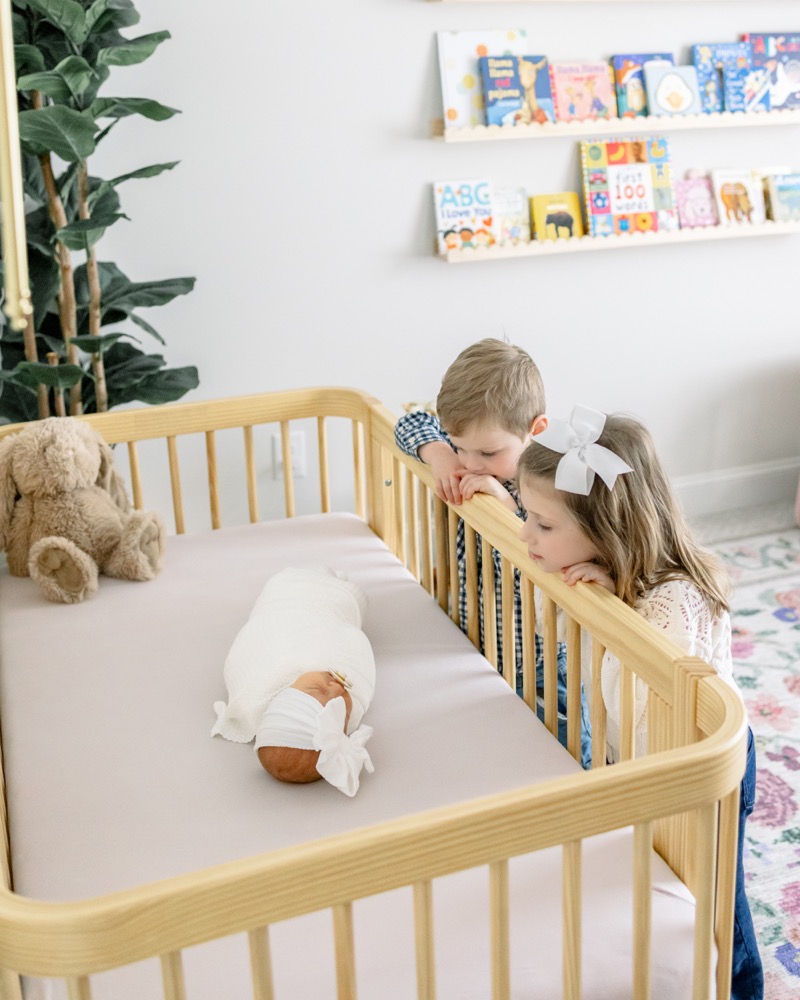 Older siblings looking lovingly into their newborn sister's crib